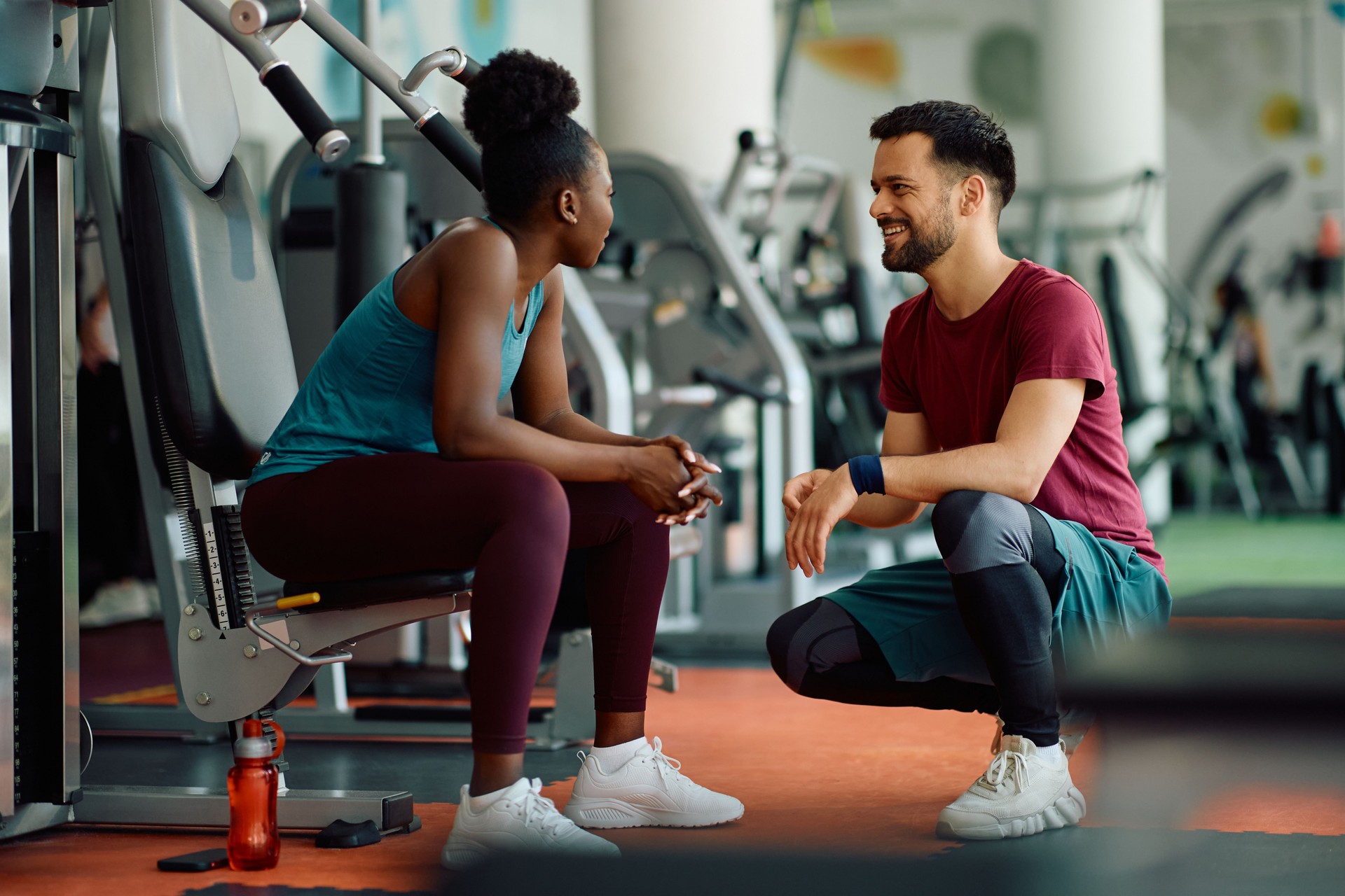 Happy athletic couple communicating while resting after working out in a gym.